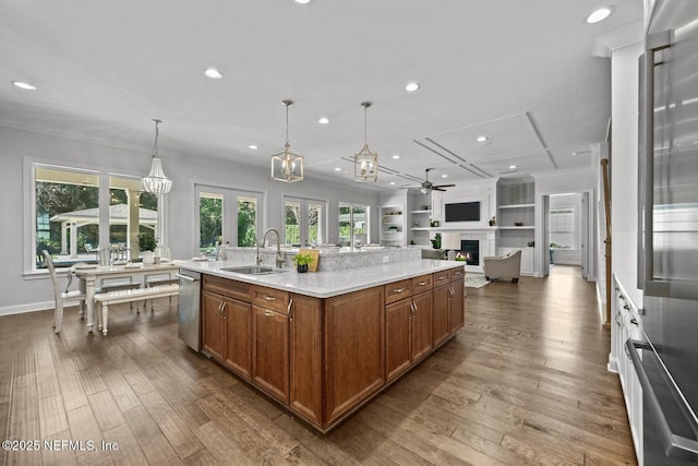 kitchen with sink, light stone counters, decorative light fixtures, a center island with sink, and ceiling fan with notable chandelier