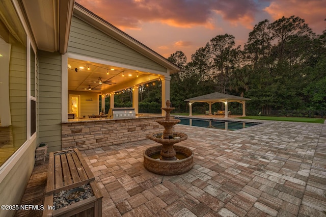 patio terrace at dusk with a gazebo, ceiling fan, and exterior kitchen