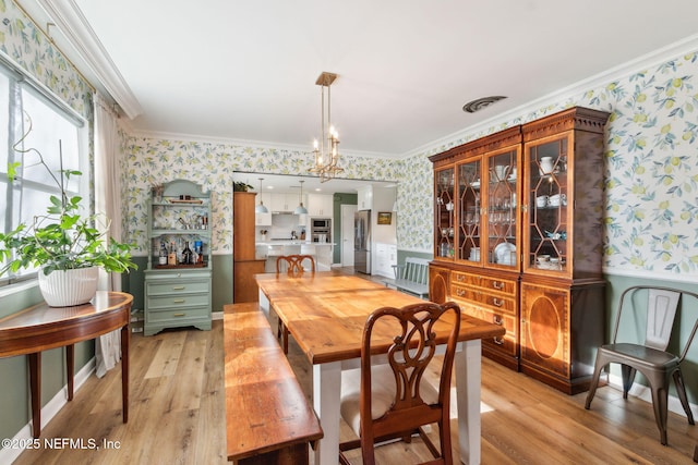 dining area with crown molding, a notable chandelier, and light wood-type flooring