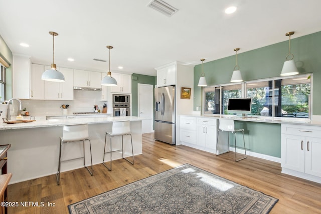 kitchen featuring white cabinets, appliances with stainless steel finishes, light hardwood / wood-style floors, and a breakfast bar area