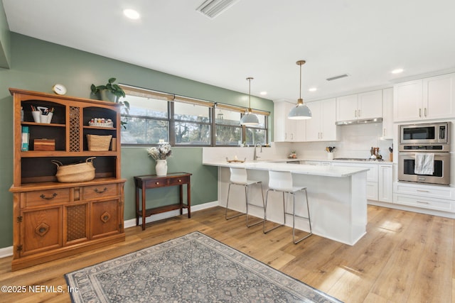 kitchen featuring white cabinets, decorative light fixtures, stainless steel appliances, and kitchen peninsula