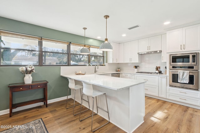 kitchen with white cabinets, appliances with stainless steel finishes, light stone countertops, and hanging light fixtures