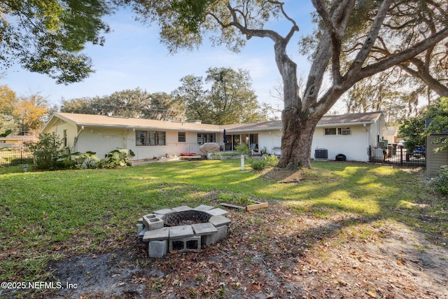 rear view of house featuring central air condition unit, a lawn, and a fire pit