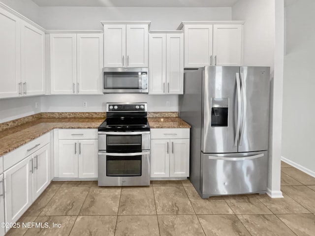 kitchen featuring dark stone counters, white cabinets, stainless steel appliances, and light tile patterned floors