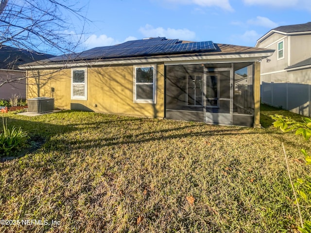 back of property with a sunroom, solar panels, a yard, and central AC