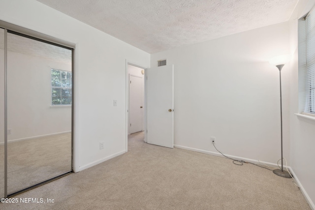 unfurnished bedroom featuring a textured ceiling, light carpet, and a closet