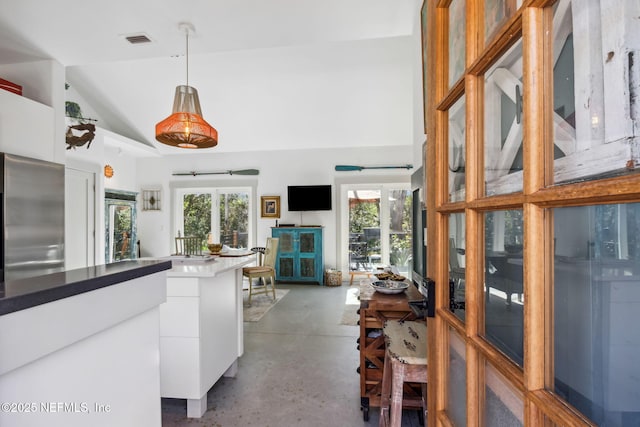 kitchen with stainless steel fridge, concrete flooring, vaulted ceiling, pendant lighting, and white cabinetry