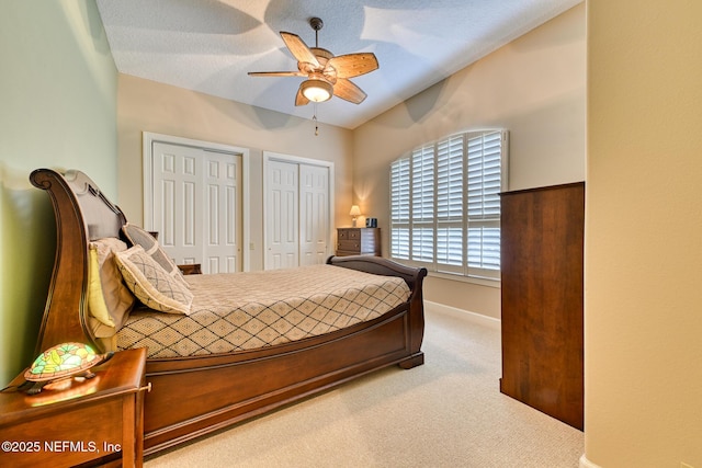 bedroom featuring a textured ceiling, ceiling fan, carpet floors, and multiple closets