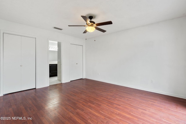 unfurnished bedroom featuring dark wood-type flooring, ceiling fan, ensuite bathroom, and multiple closets