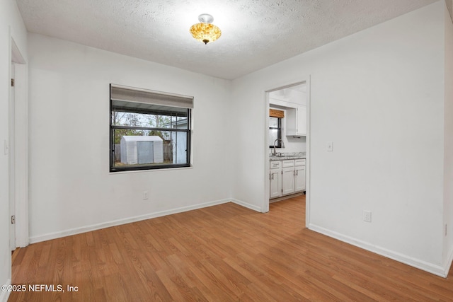 unfurnished room featuring a textured ceiling, light wood-type flooring, and sink