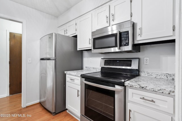 kitchen featuring stainless steel appliances, white cabinetry, light hardwood / wood-style floors, and light stone countertops