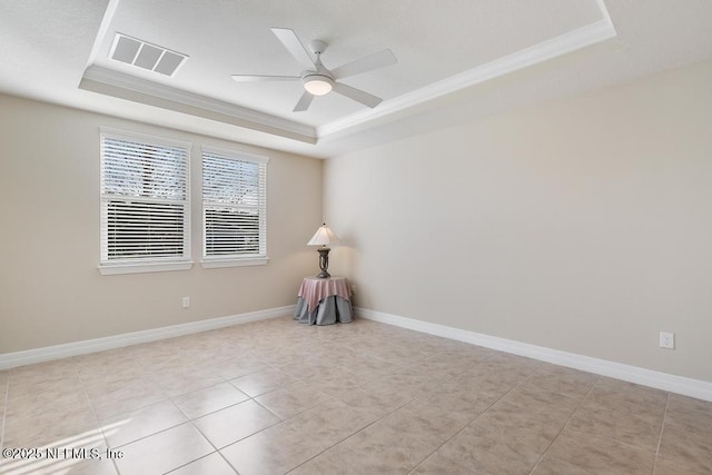 tiled empty room with ceiling fan, a raised ceiling, and ornamental molding