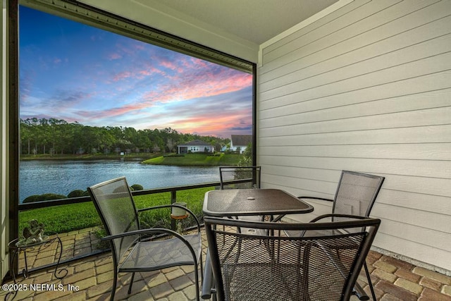 balcony at dusk featuring a water view