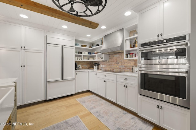 kitchen featuring stainless steel double oven, white cabinets, wall chimney exhaust hood, paneled built in refrigerator, and light hardwood / wood-style floors