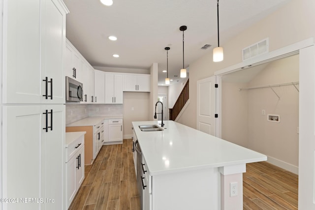 kitchen featuring white cabinets, sink, hanging light fixtures, an island with sink, and stainless steel appliances