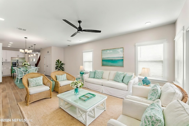 living room featuring ceiling fan with notable chandelier and light wood-type flooring