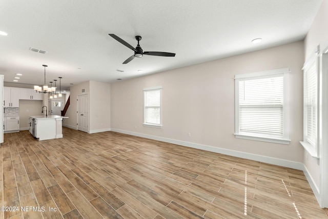 unfurnished living room with sink and ceiling fan with notable chandelier