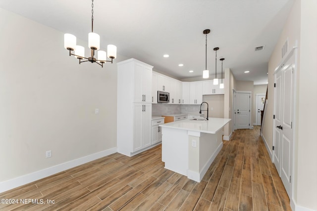 kitchen featuring decorative light fixtures, white cabinetry, an island with sink, and a chandelier