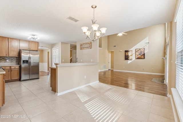 kitchen with an inviting chandelier, tasteful backsplash, stainless steel fridge, pendant lighting, and light tile patterned floors