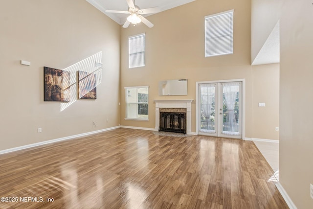 unfurnished living room with ceiling fan, a high end fireplace, a towering ceiling, and light wood-type flooring