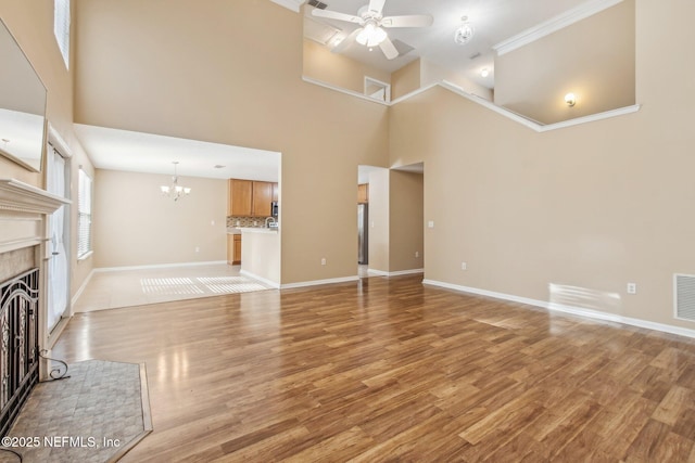 unfurnished living room featuring ceiling fan with notable chandelier, a towering ceiling, light hardwood / wood-style flooring, and a tiled fireplace