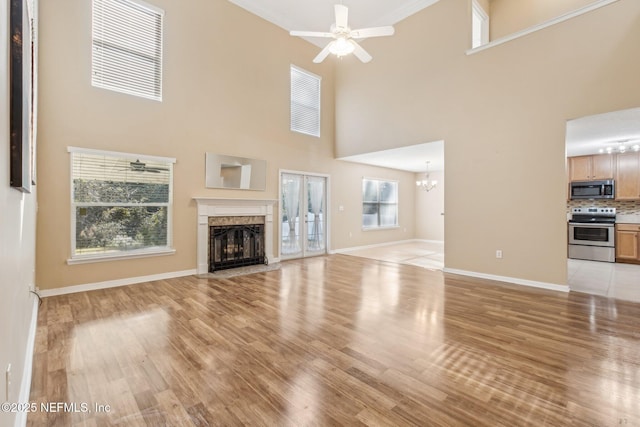 unfurnished living room featuring ceiling fan with notable chandelier, light hardwood / wood-style floors, and a high ceiling