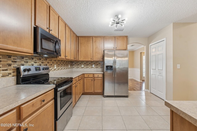 kitchen with light tile patterned floors, a textured ceiling, appliances with stainless steel finishes, tasteful backsplash, and a chandelier