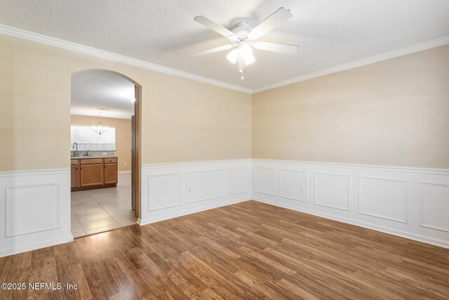 unfurnished room with a textured ceiling, ceiling fan with notable chandelier, light hardwood / wood-style floors, and crown molding