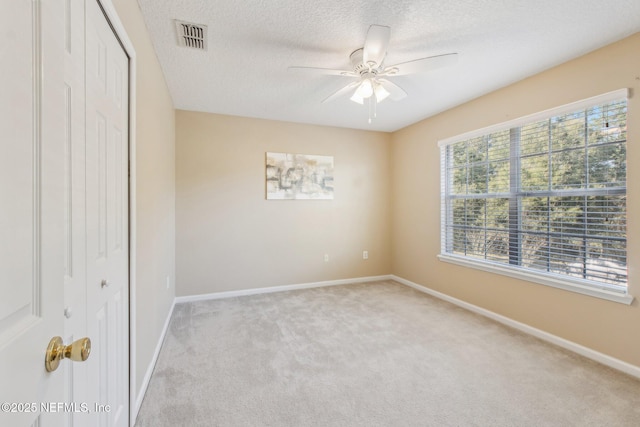 empty room featuring a textured ceiling, light colored carpet, and ceiling fan