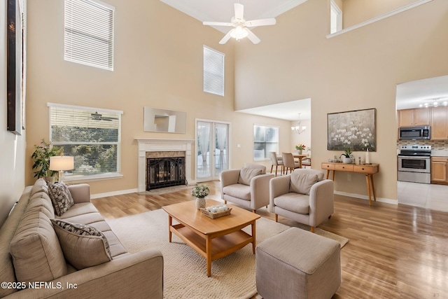 living room with a tiled fireplace, light hardwood / wood-style flooring, a high ceiling, and ceiling fan with notable chandelier