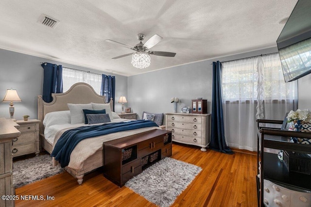 bedroom with ceiling fan, ornamental molding, a textured ceiling, and light wood-type flooring