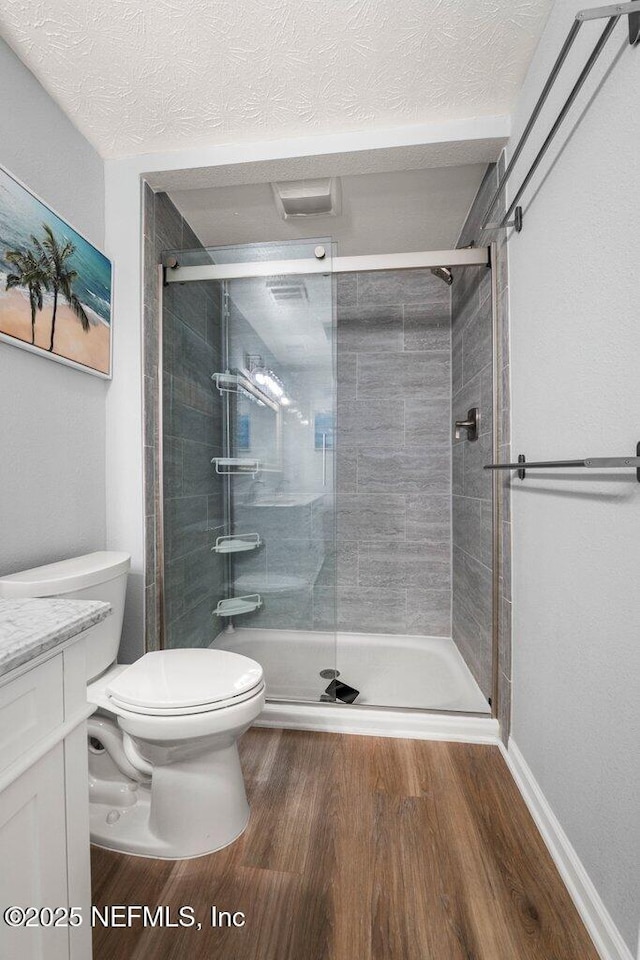 bathroom with walk in shower, vanity, a textured ceiling, hardwood / wood-style floors, and toilet