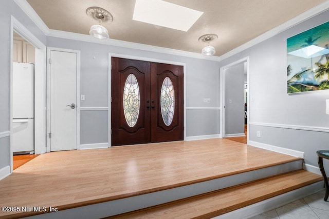 tiled entrance foyer with french doors, a skylight, and crown molding