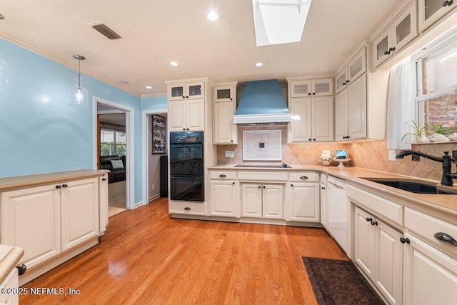 kitchen featuring pendant lighting, custom exhaust hood, black appliances, sink, and a skylight