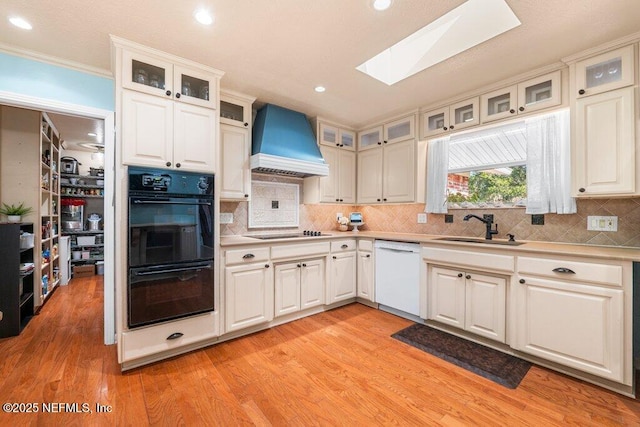 kitchen with a skylight, white cabinetry, sink, premium range hood, and black appliances