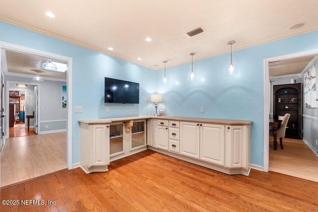 kitchen with decorative light fixtures, white cabinetry, light wood-type flooring, and crown molding