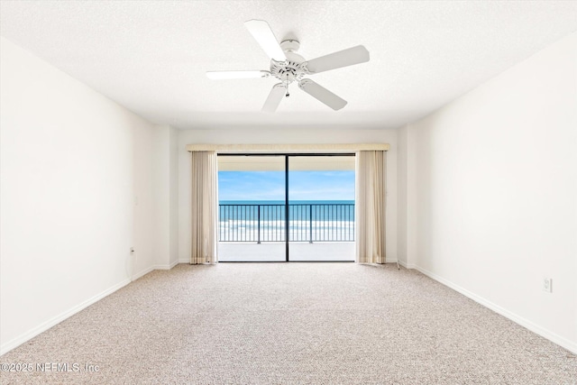 empty room with a textured ceiling, carpet floors, a water view, and ceiling fan