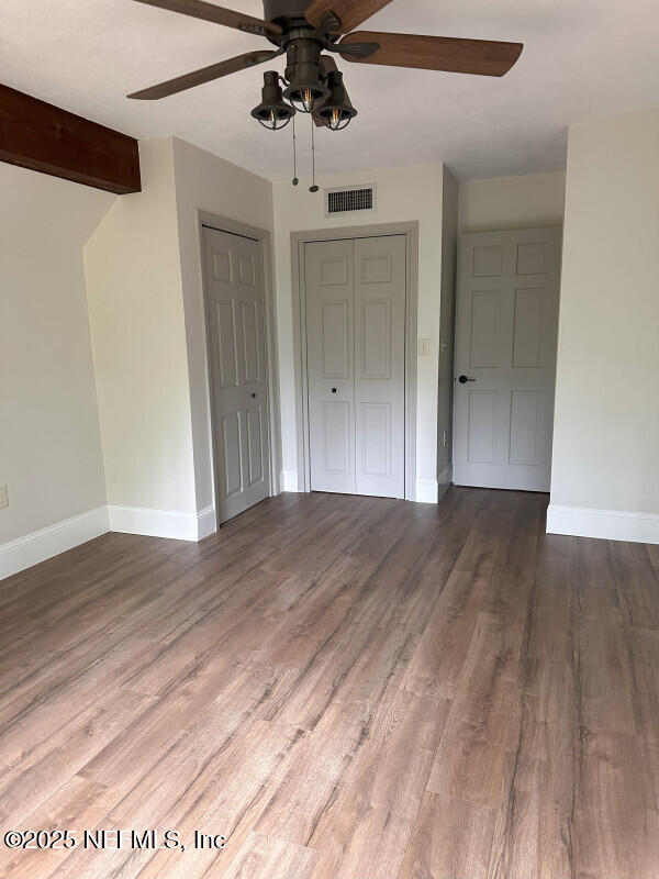 unfurnished bedroom featuring beam ceiling, dark hardwood / wood-style flooring, a closet, and ceiling fan