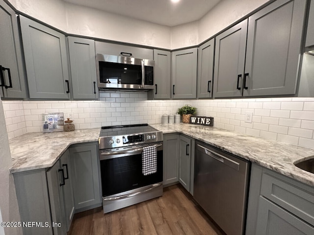 kitchen featuring gray cabinetry, dark hardwood / wood-style floors, light stone countertops, and stainless steel appliances