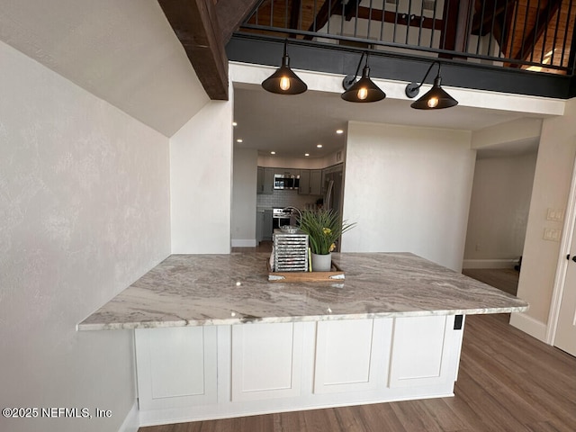 kitchen with dark hardwood / wood-style floors, light stone countertops, kitchen peninsula, and appliances with stainless steel finishes