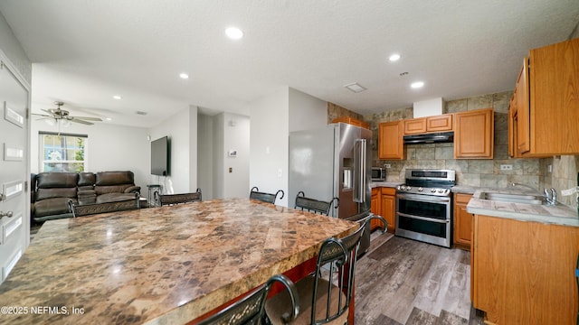 kitchen featuring ceiling fan, sink, stainless steel appliances, decorative backsplash, and light wood-type flooring