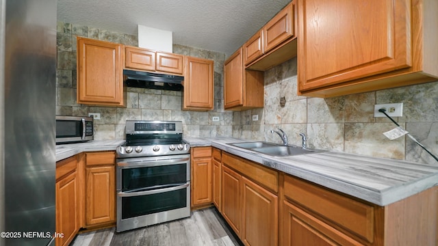 kitchen with sink, decorative backsplash, a textured ceiling, light hardwood / wood-style floors, and stainless steel appliances