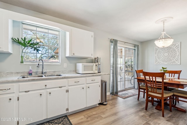 kitchen with sink, light hardwood / wood-style flooring, a chandelier, pendant lighting, and white cabinets