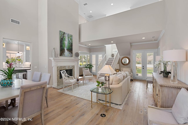 living room with french doors, crown molding, a premium fireplace, and light wood-type flooring