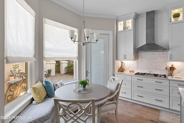 kitchen with wall chimney exhaust hood, stainless steel gas cooktop, crown molding, decorative light fixtures, and white cabinets