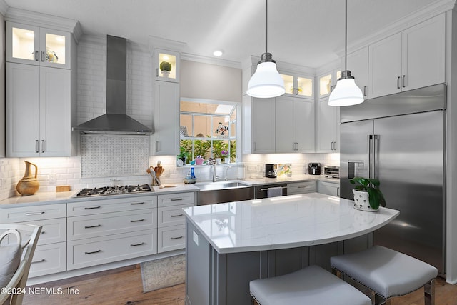 kitchen featuring a breakfast bar, appliances with stainless steel finishes, a kitchen island, wall chimney range hood, and white cabinets