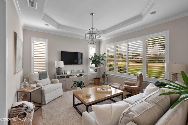 living room with an inviting chandelier, plenty of natural light, light hardwood / wood-style floors, and a raised ceiling