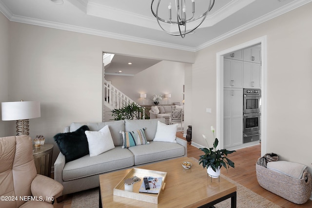 living room featuring crown molding, a chandelier, a raised ceiling, and light wood-type flooring