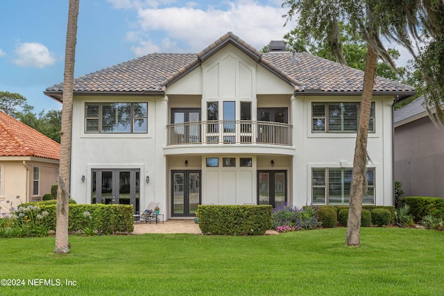 rear view of property featuring a balcony, a lawn, and french doors