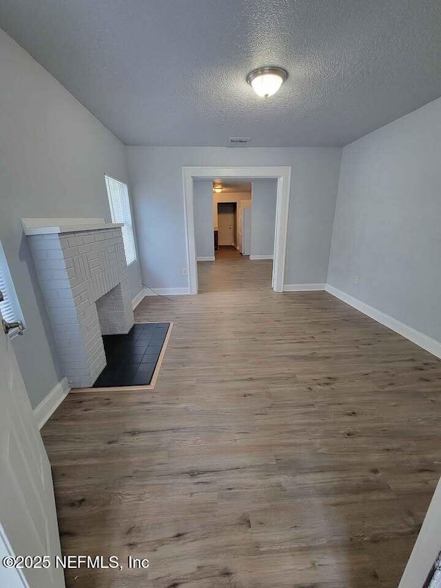 unfurnished living room with hardwood / wood-style flooring, a textured ceiling, and a brick fireplace